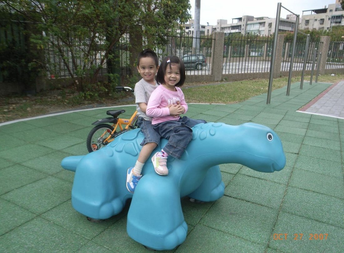 Gwyneth as a child with her older brother, riding a blue dinosaur at a Taiwanese playground, October 2007.